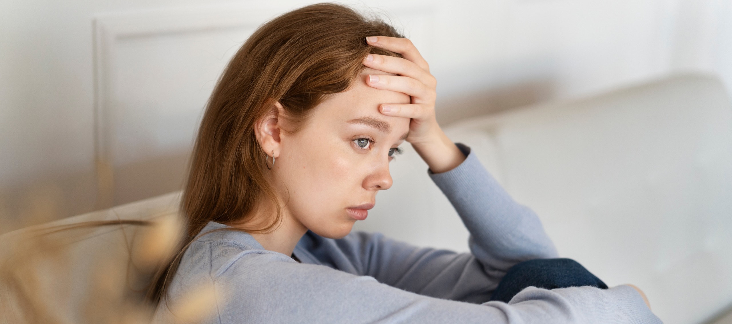 An anxious woman sits on the couch staring off into the distance.